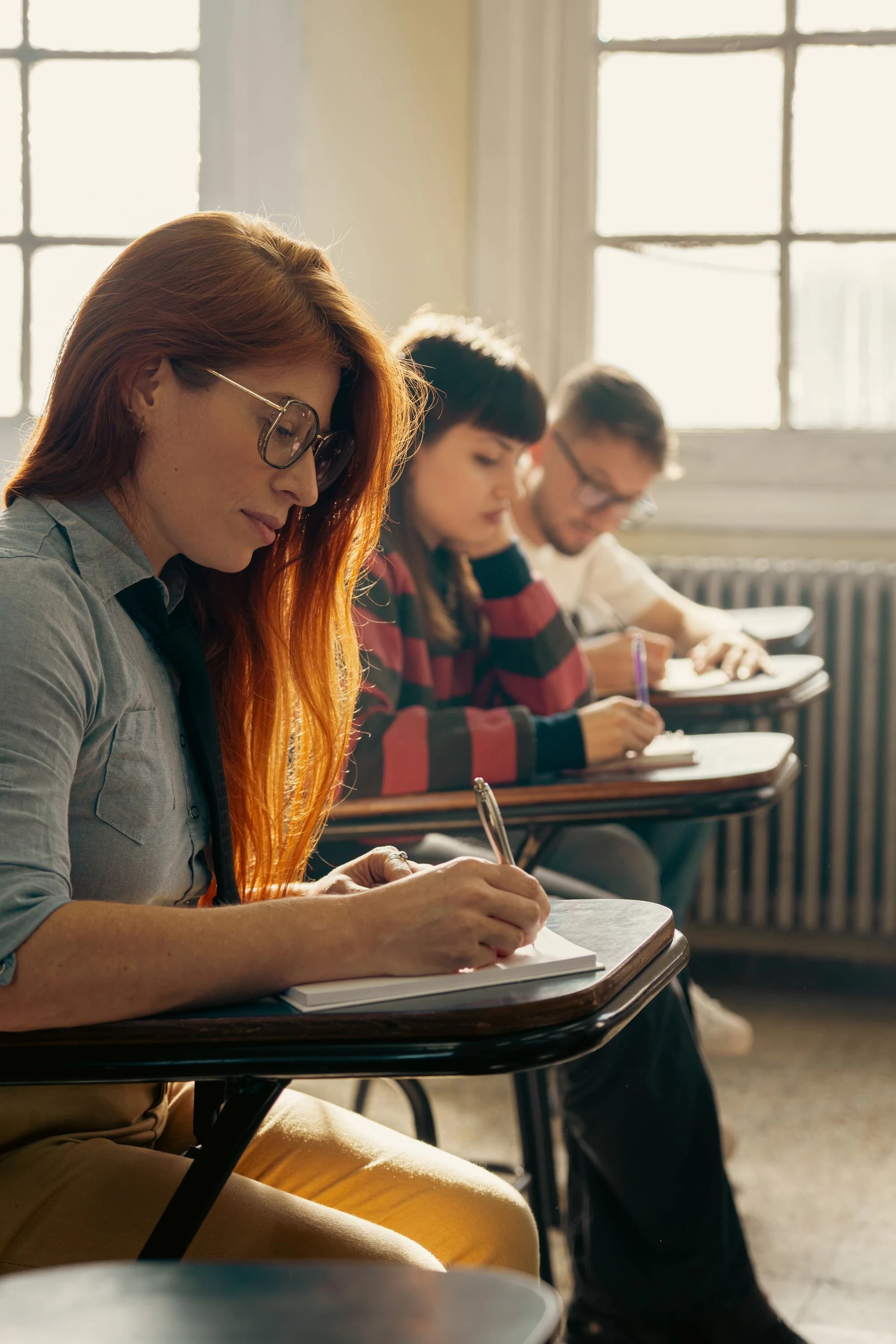 Adult learners around a warm classroom table taking notes with their instructor.