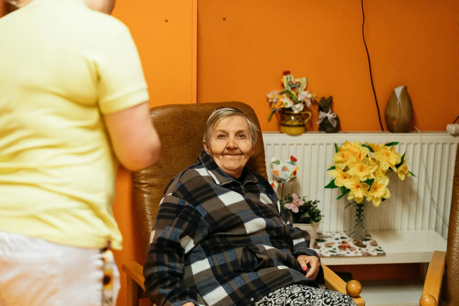 A Polaris Gateway carer sits beside an older woman in a warm sitting room, in quiet conversation.