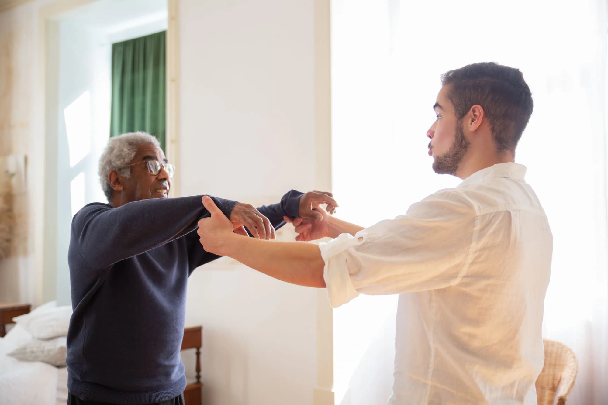 A care worker holds an older man's hand in quiet conversation at home.
