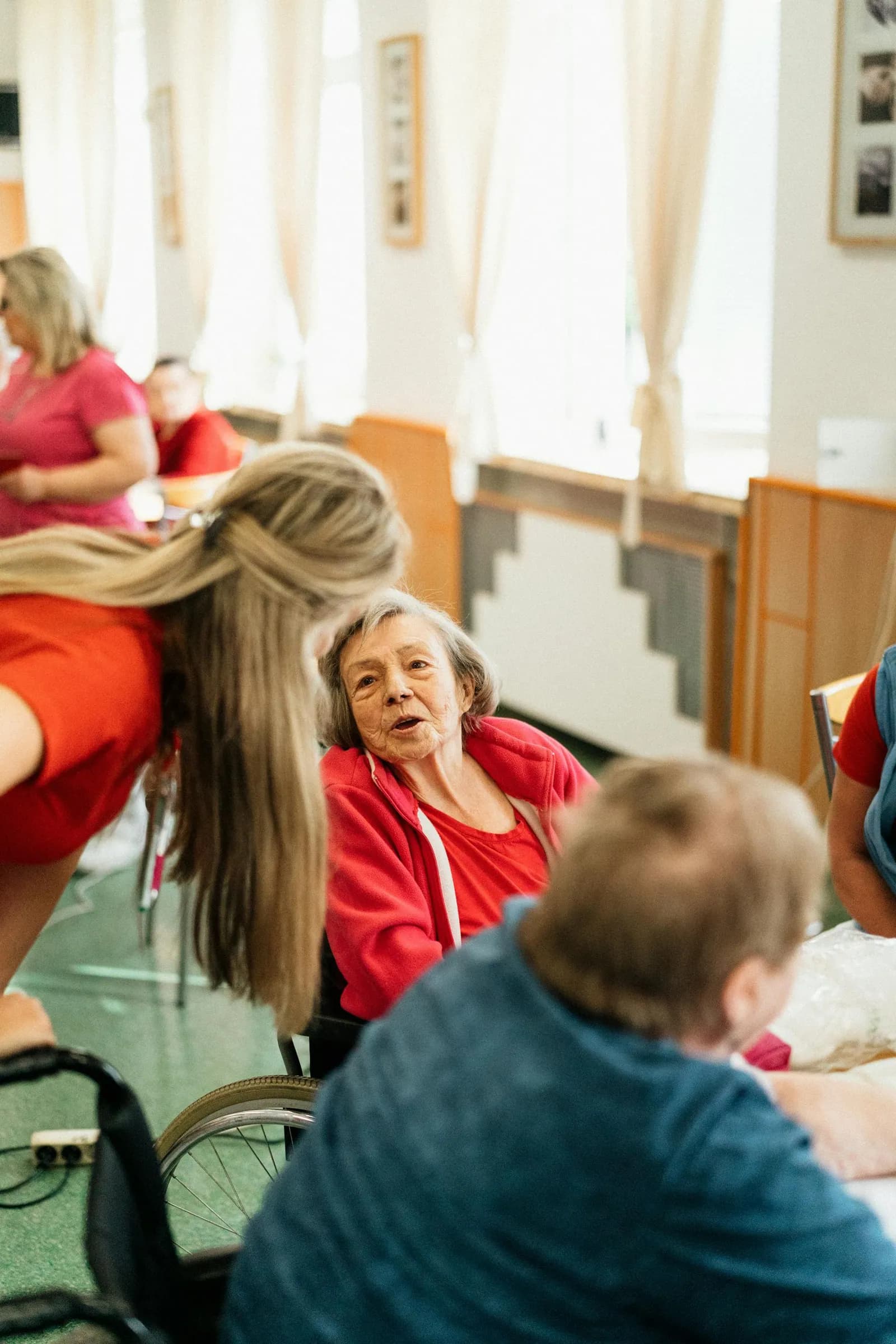 A Polaris Gateway carer chats with an older woman in her wheelchair, light streaming through the window behind them.