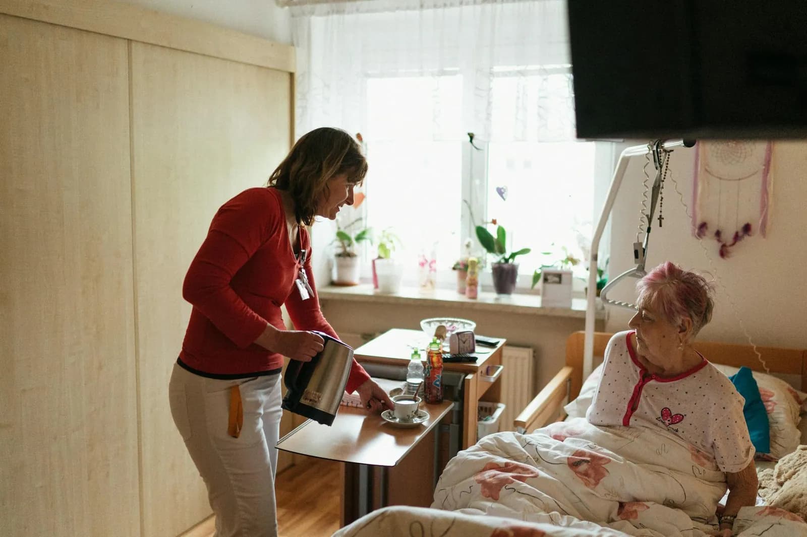 A carer serves tea to an older woman in her own bedroom, a small daily ritual at the heart of domiciliary care.
